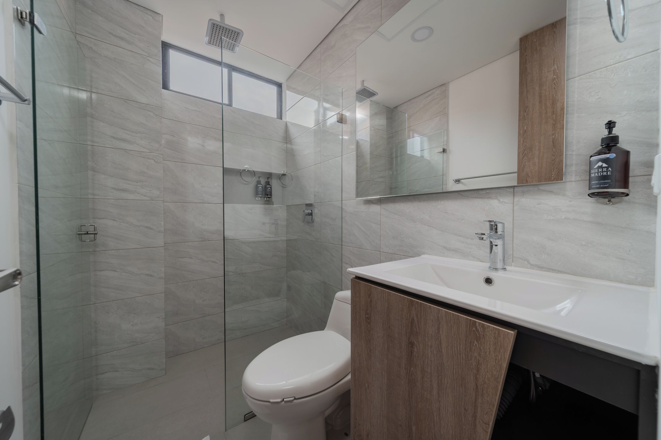 A modern bathroom with a glass shower enclosure, a white toilet, and a sink with a wooden cabinet.