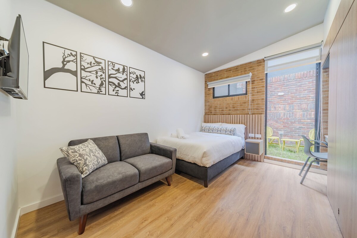 Un dormitorio moderno con un sofá gris, una cama con ropa blanca y una pared de ladrillo.