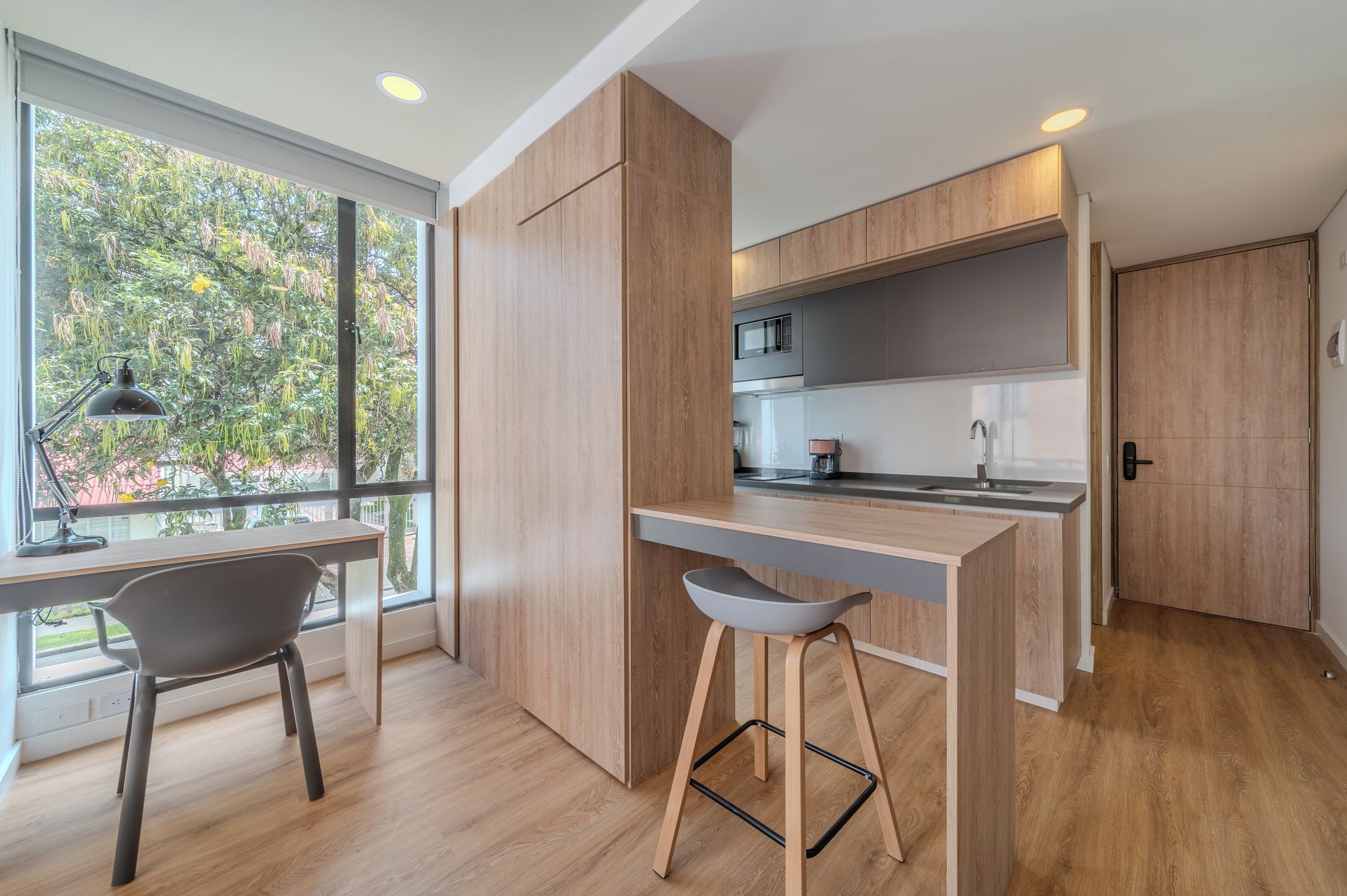 A modern kitchen with wooden cabinets, a built-in microwave, and a bar area with stools.