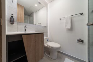 Un baño moderno con inodoro blanco, tocador de madera, cabina de ducha con mampara de vidrio y un perchero para toallas.