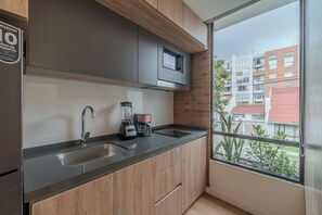 A modern kitchen with a large window, stainless steel appliances, and wooden cabinets. -  Sierra Madre Apartamentos (Bogotá)