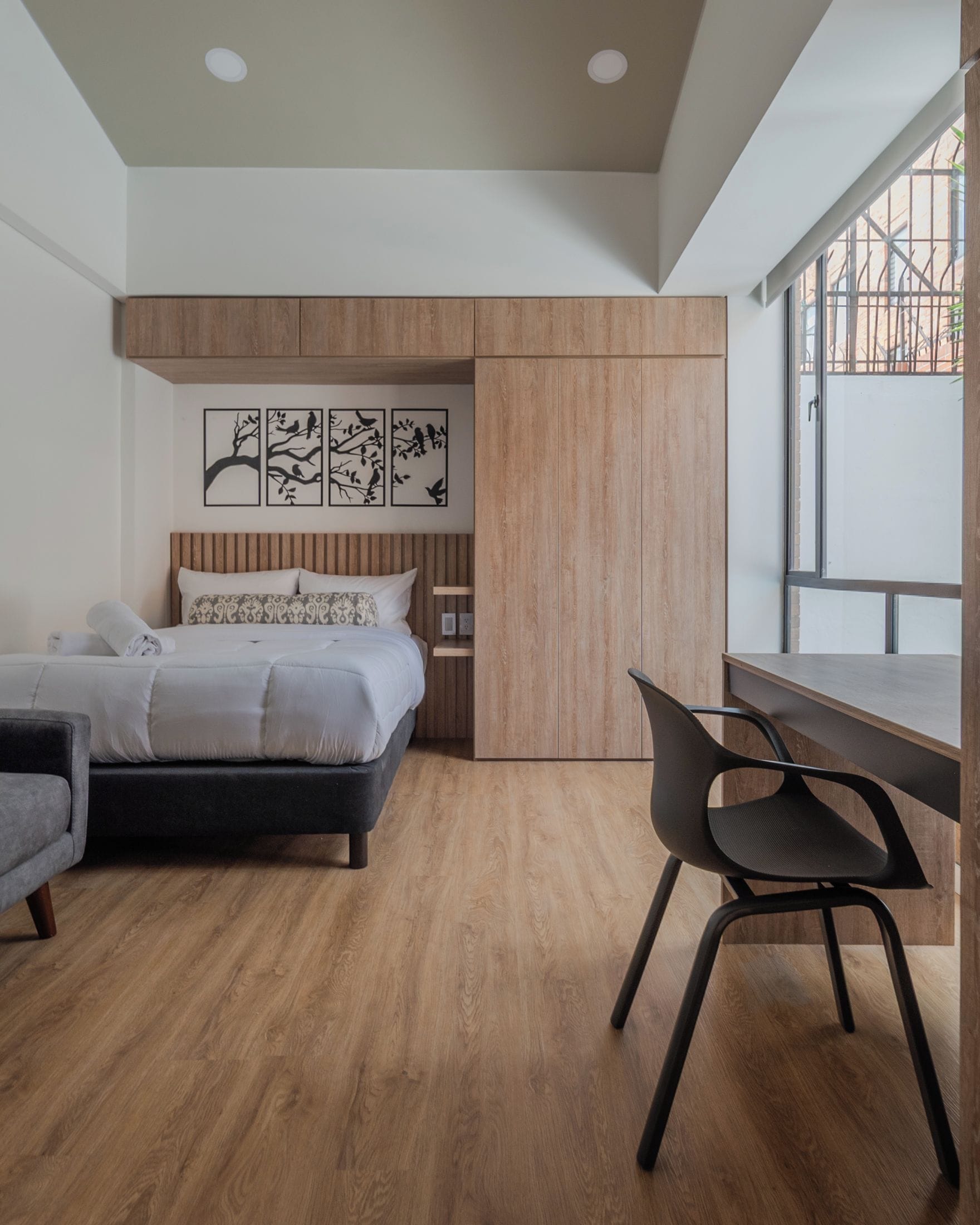 A modern bedroom with a bed, a desk, and a chair. There are wall art pieces above the bed.