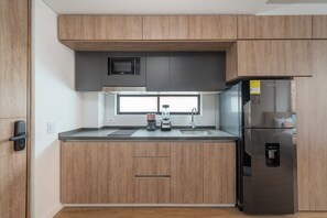 Una cocina moderna con armarios de madera, un refrigerador de acero inoxidable, un microondas integrado y una cafetera.