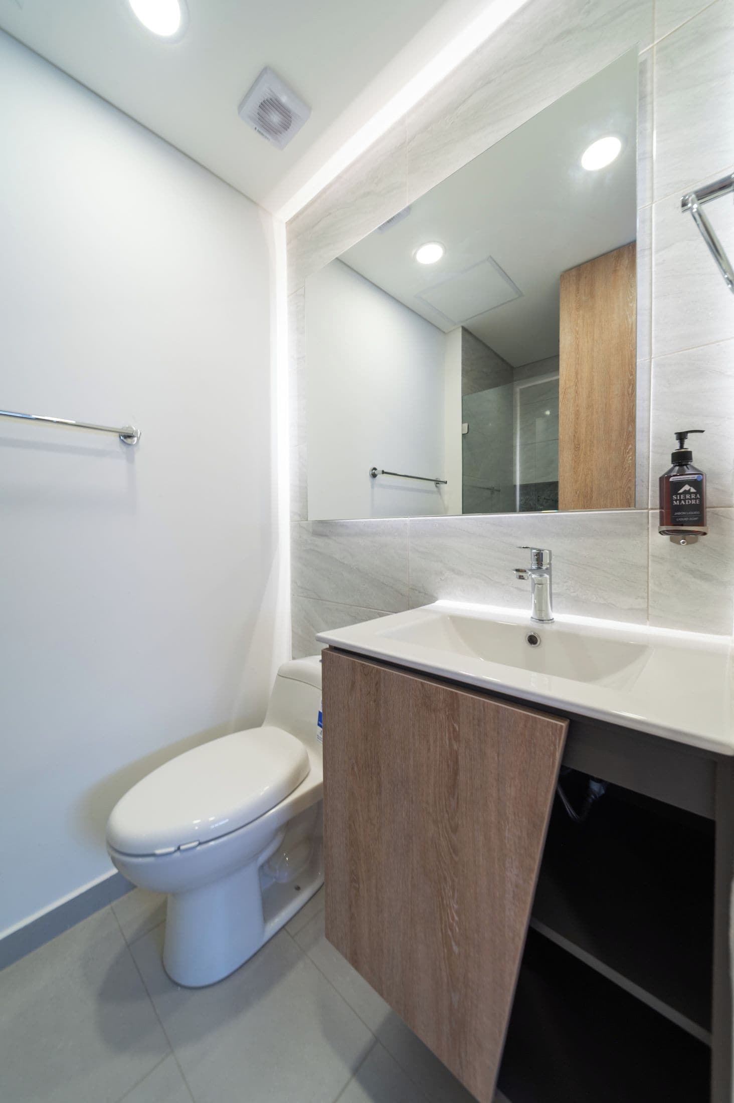 Une salle de bain moderne avec des toilettes blanches, un lavabo doté d’un meuble en bois et un miroir au-dessus du lavabo.