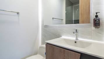 Une salle de bain moderne avec des toilettes blanches, un lavabo doté d’un meuble en bois et un miroir au-dessus du lavabo.