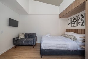 A bedroom with a bed, a sofa, a mounted TV, and a wooden headboard. -  Sierra Madre Apartamentos (Bogotá)