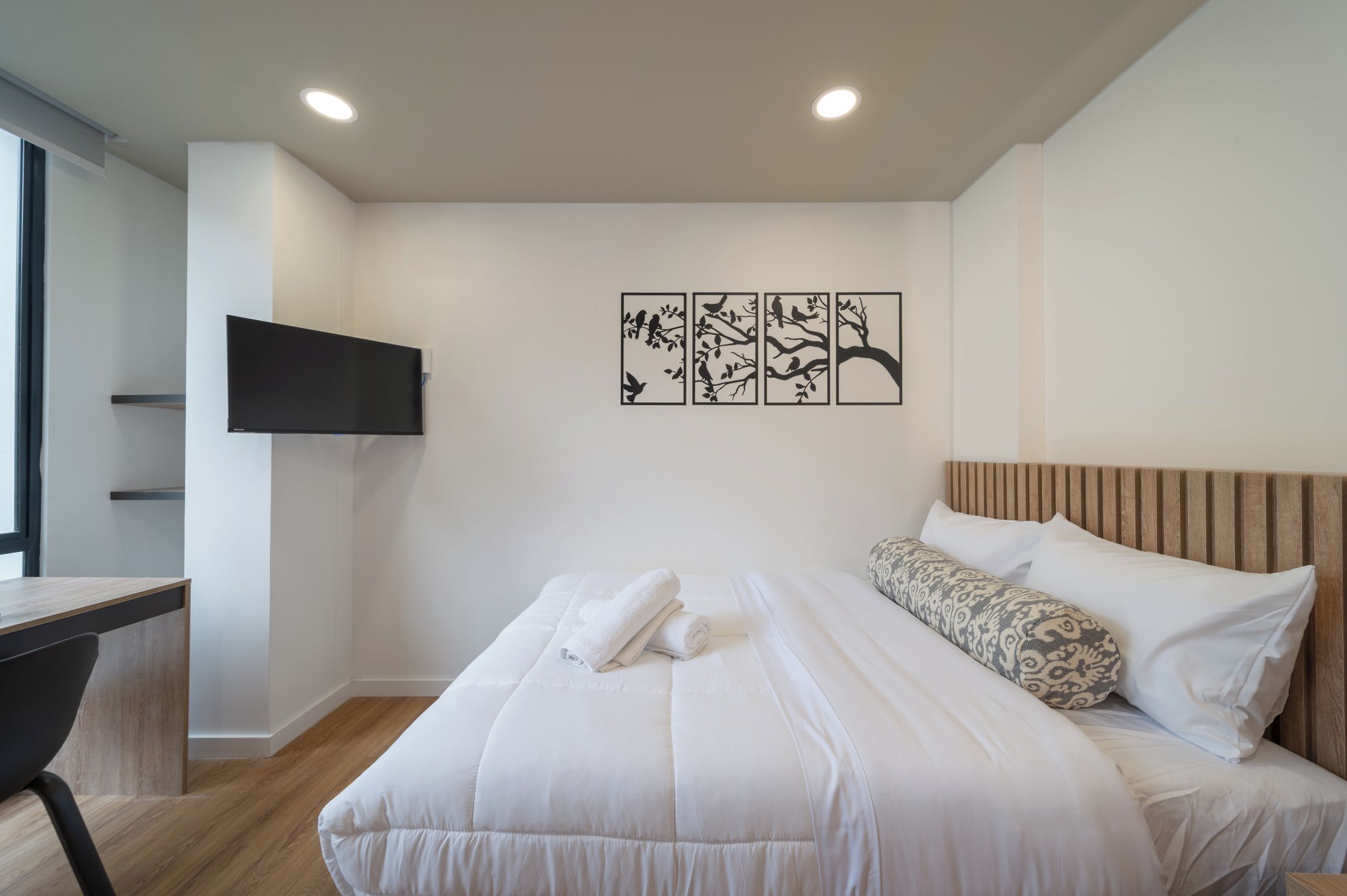 A modern bedroom with a bed, a desk, and a mounted TV.
