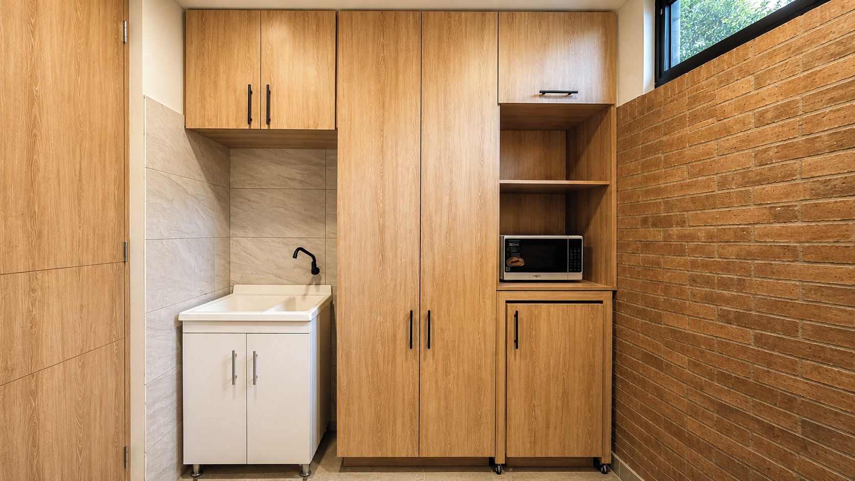 Una cocina compacta con armarios de madera, un lavamanos blanco y un microondas en un estante.