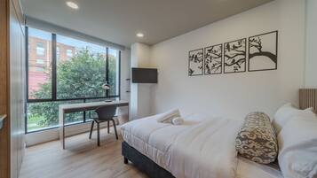 A modern bedroom with a large bed, a desk, and a window.
