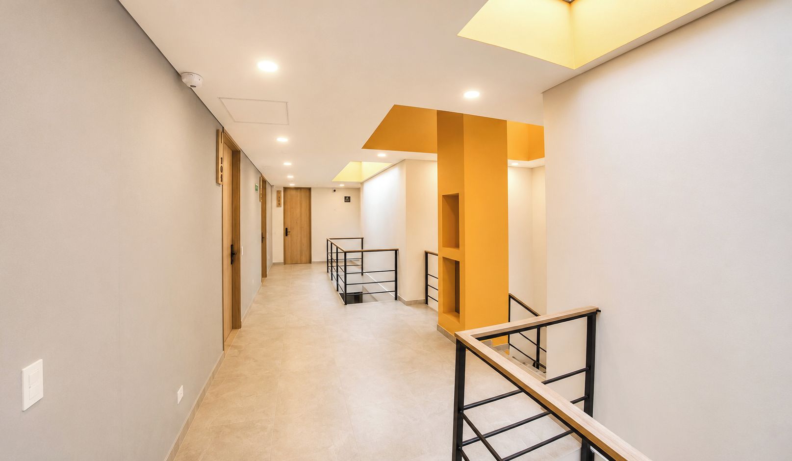 Un pasillo con piso de madera, una escalera con barandilla de metal e iluminación empotrada.