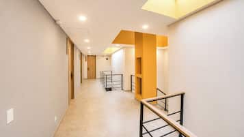 Un pasillo con piso de madera, una escalera con barandilla de metal e iluminación empotrada.