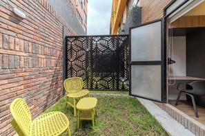 Un pequeño espacio al aire libre con sillas amarillas y una mesa, delimitado por una valla decorativa negra.