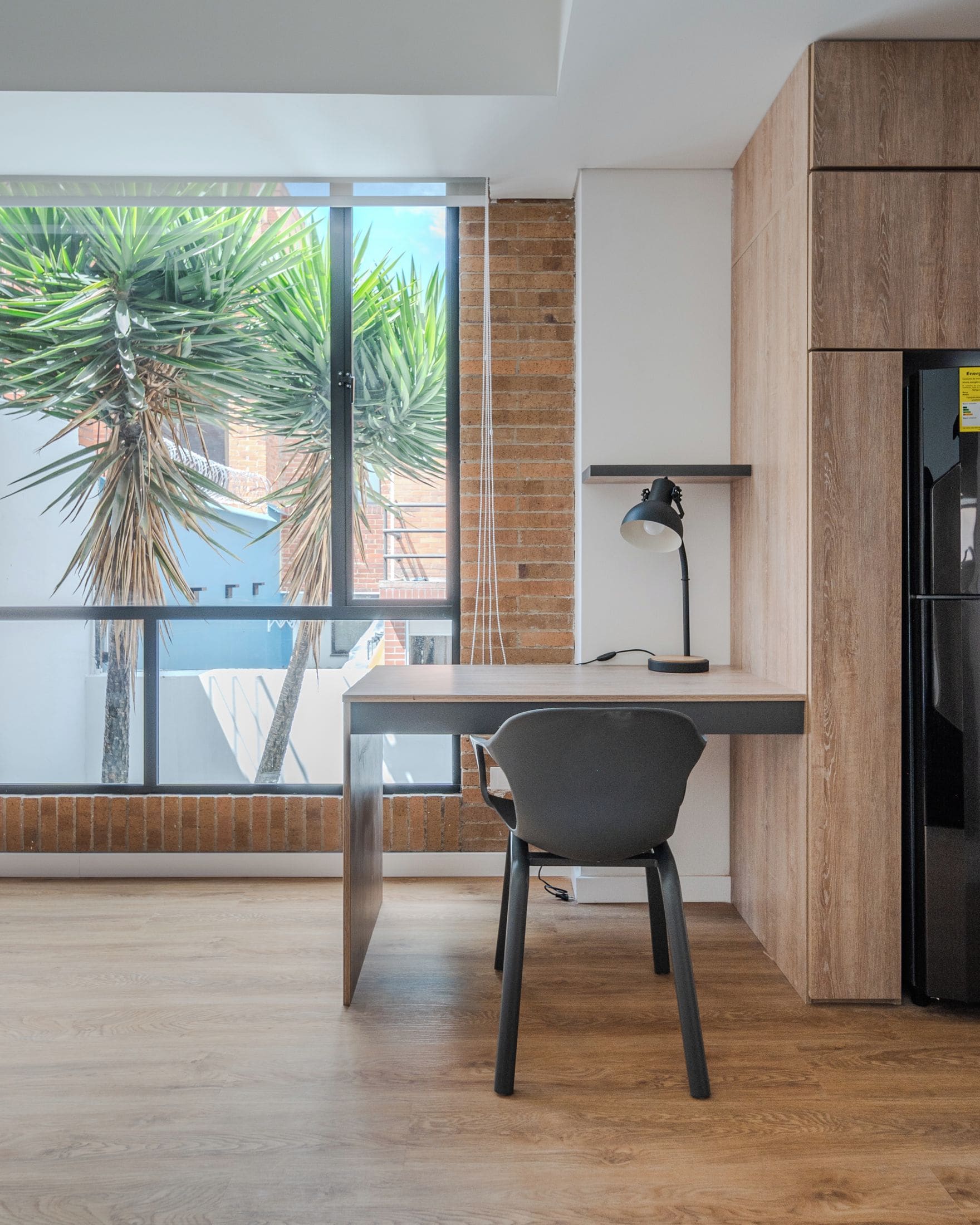 A modern kitchen with a wooden cabinet, a black refrigerator, and a desk with a chair.