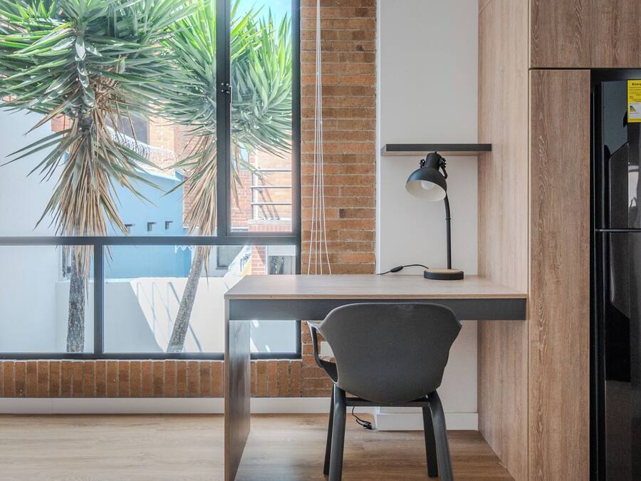 A modern kitchen with a wooden cabinet, a black refrigerator, and a desk with a chair.