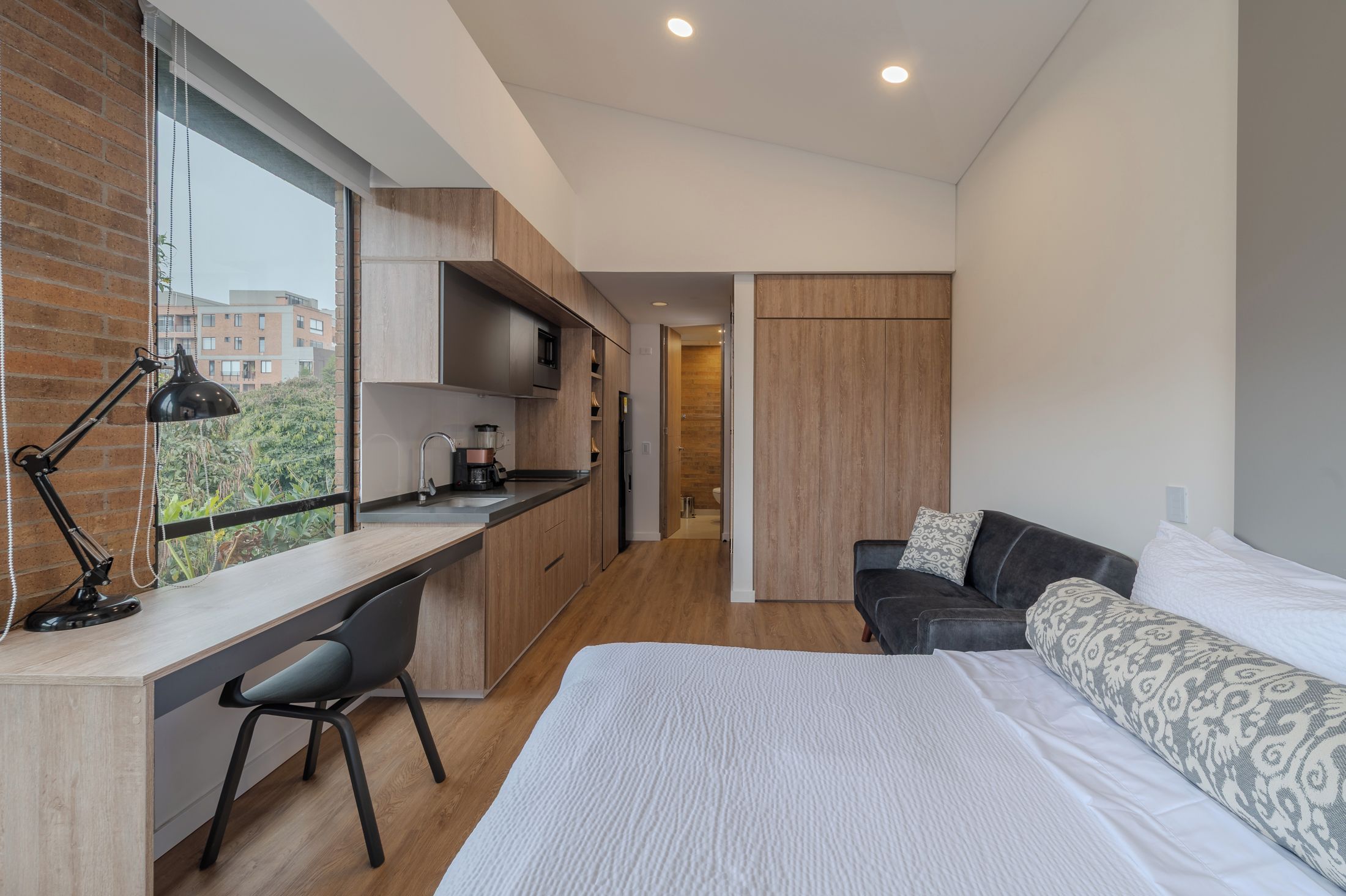 Een moderne slaapkamer met een groot bed, een bureau en een bank. Een raam biedt uitzicht op het omliggende landschap.