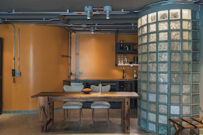 Una cocina con una mesa de madera, taburetes de bar y un separador de vidrio.