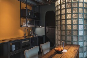 Una cocina compacta con zona de comedor, que incluye una mesa de madera, sillas, un bol de frutas y un soporte para copas de vino.