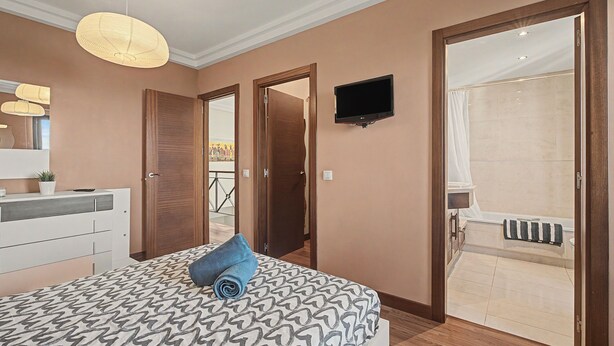Quarto com cama, televisão fixada na parede e banheiro com banheira.