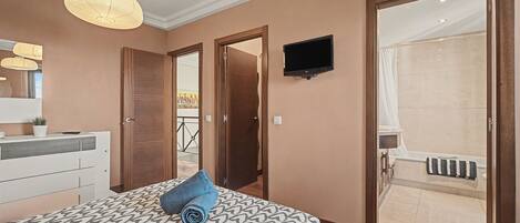 Un dormitorio con una cama, un televisor montado en la pared y un baño con bañera.