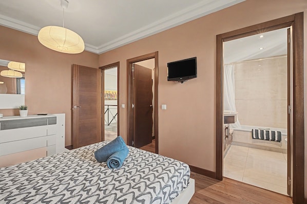 Une chambre à coucher avec un lit, un téléviseur fixé au mur et une salle de bain avec une baignoire.