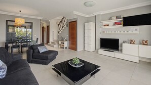 Uma sala de estar moderna com uma mesa de centro preta, sofás cinzentos, uma TV e uma lareira.