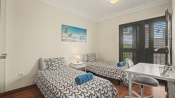 A room with two beds, a desk, a chair, and a window with blinds.