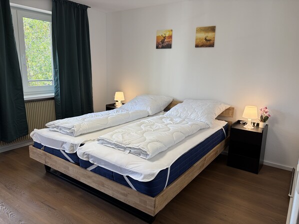 A double bed with white bedding, two bedside lamps, and a window with curtains.