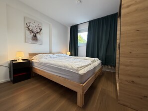 Une chambre à coucher avec un lit en bois, une table de chevet, une lampe, un tableau décoratif au mur et une fenêtre avec des rideaux.