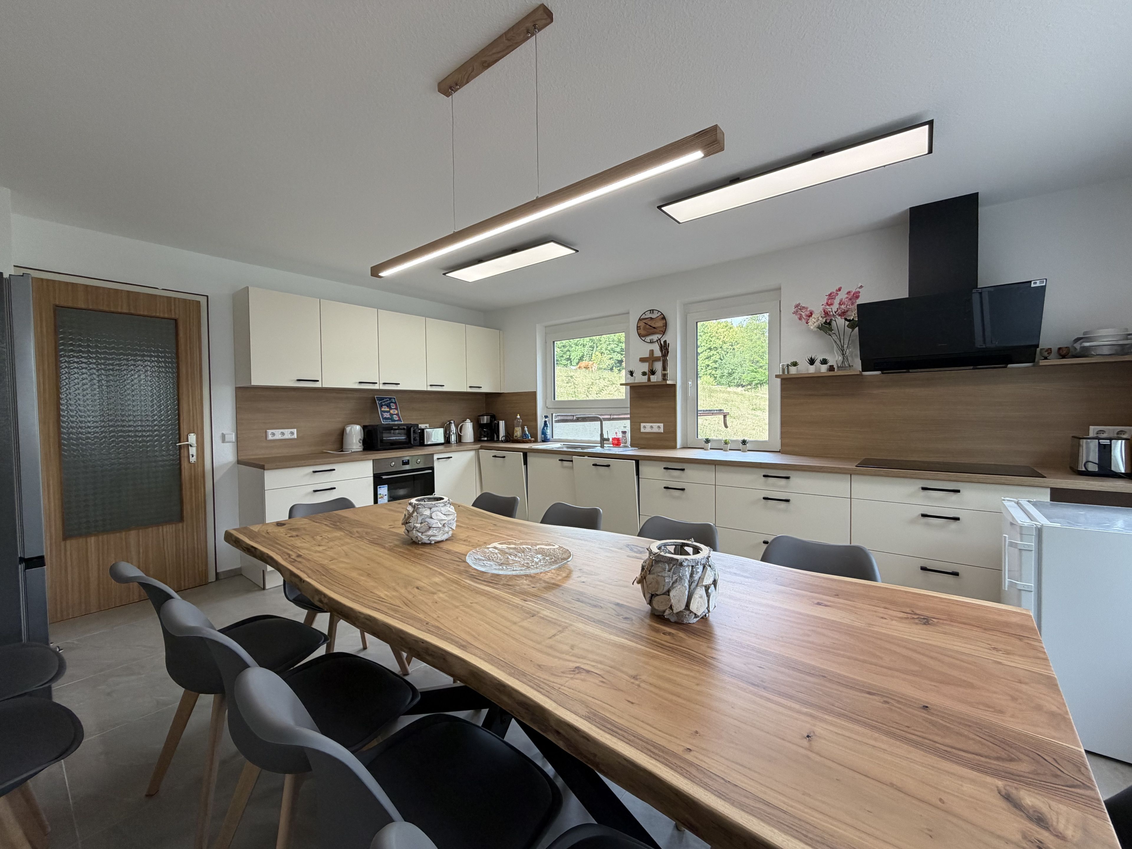 Une cuisine moderne avec une table à manger en bois, des chaises noires et des appareils électroménagers intégrés.
