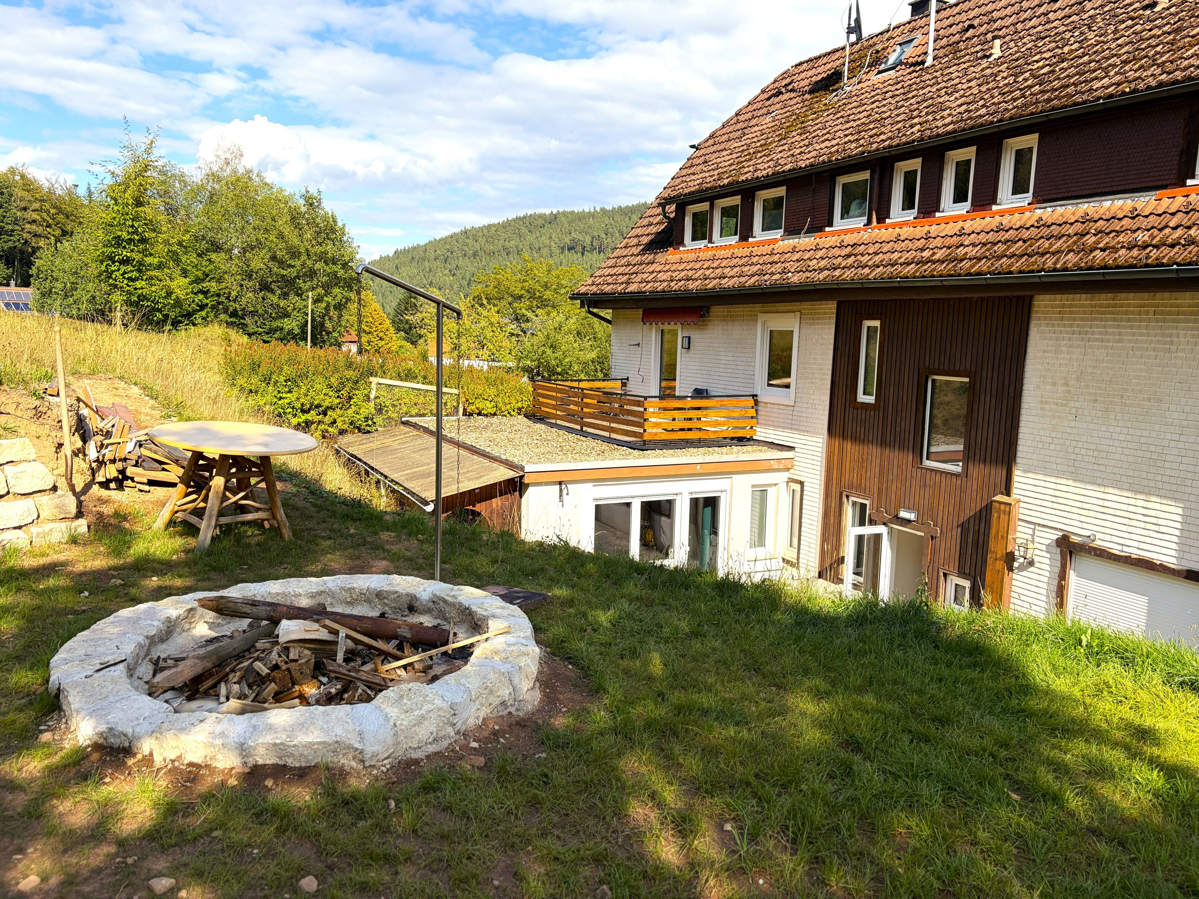 Una casa con terraza de madera, un brasero y vistas del paisaje circundante.