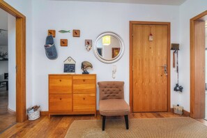 Ein Zimmer mit einem Holzkasten, einem Stuhl, einem Spiegel und einer Tür.