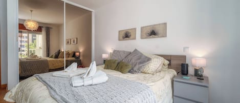 Una habitación de hotel con una cama grande, una mesita de noche con lámpara, un espejo y obras de arte en la pared.