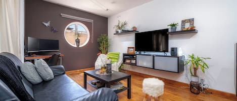 A modern living room with a leather sofa, a round mirror, a flat-screen TV, and a wooden coffee table.