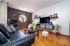 Un salon moderne avec un canapé en cuir, un miroir rond, un téléviseur à écran plat et une table basse en bois.