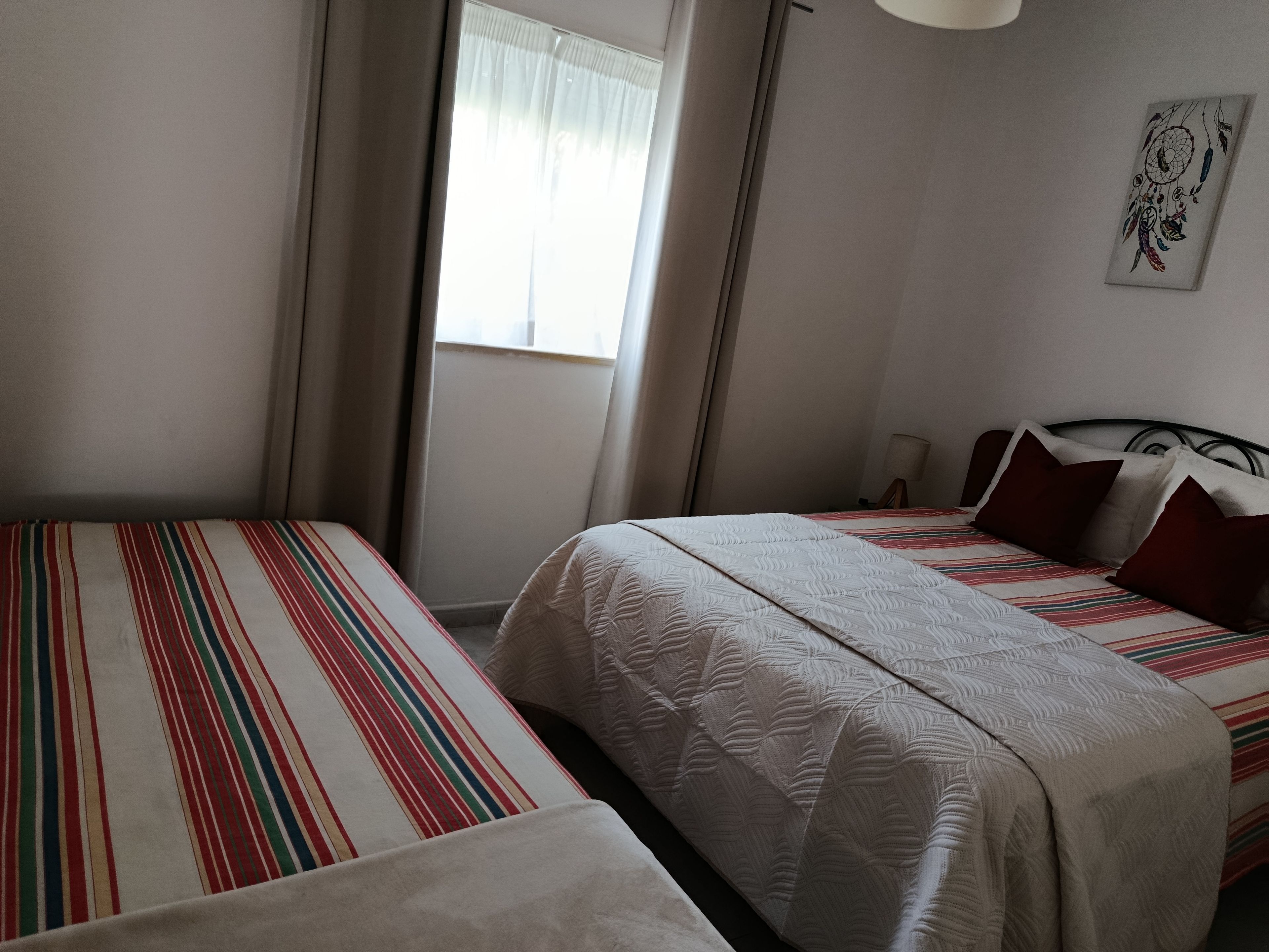 A hotel room with two beds, a window with curtains, a wall-mounted artwork, and a bedside lamp.