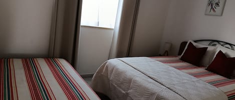 Habitación de hotel con dos camas, una ventana con cortinas, una obra de arte en la pared y una lámpara de noche.