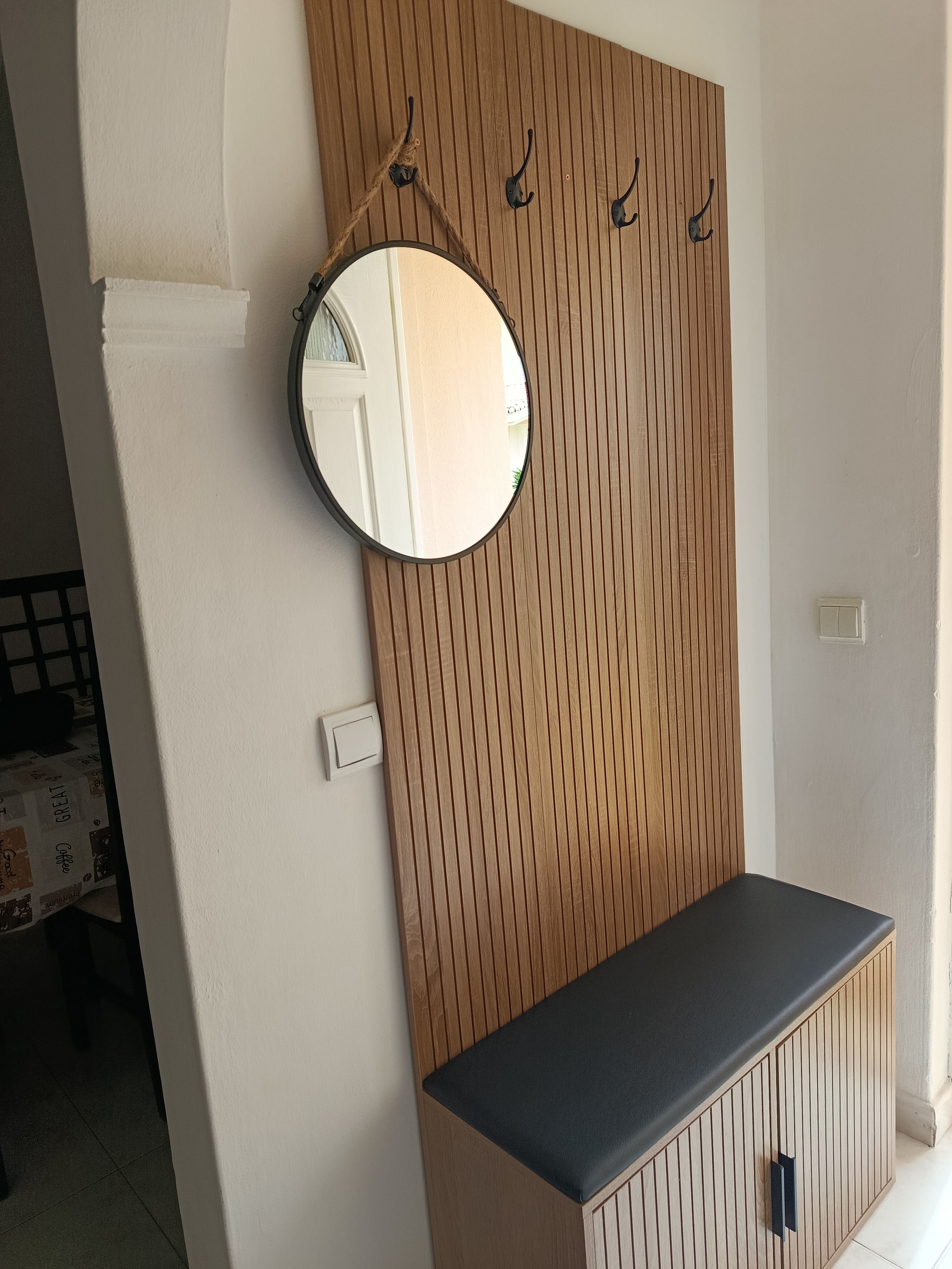 A room with a wooden panel wall, a round mirror, and a black bench.