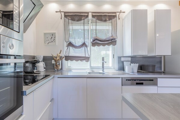 Una cocina moderna con electrodomésticos de acero inoxidable, lavavajillas y una ventana con cortinas decorativas.