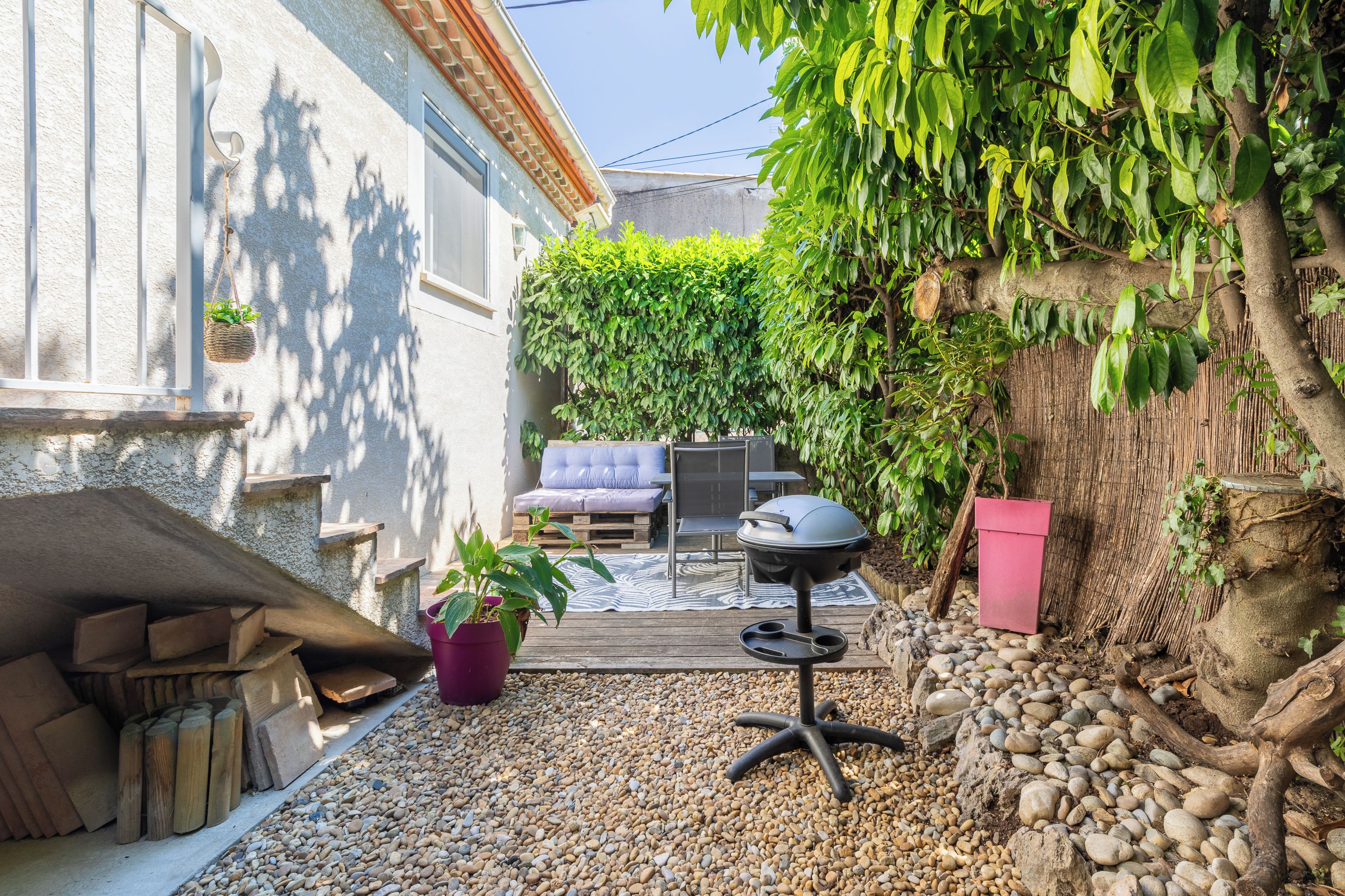 Un pati amb una barbacoa, zona de seients i una paret coberta de plantes enfilades.