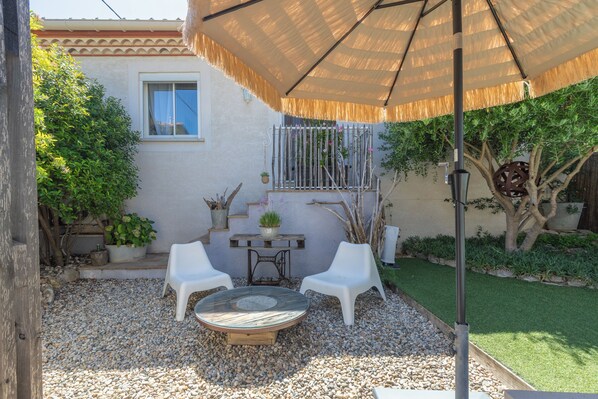 An outdoor patio with a round table, two white chairs, and a large umbrella. - Les Bois Flottès - Jardin -Climatisation (Poussan)