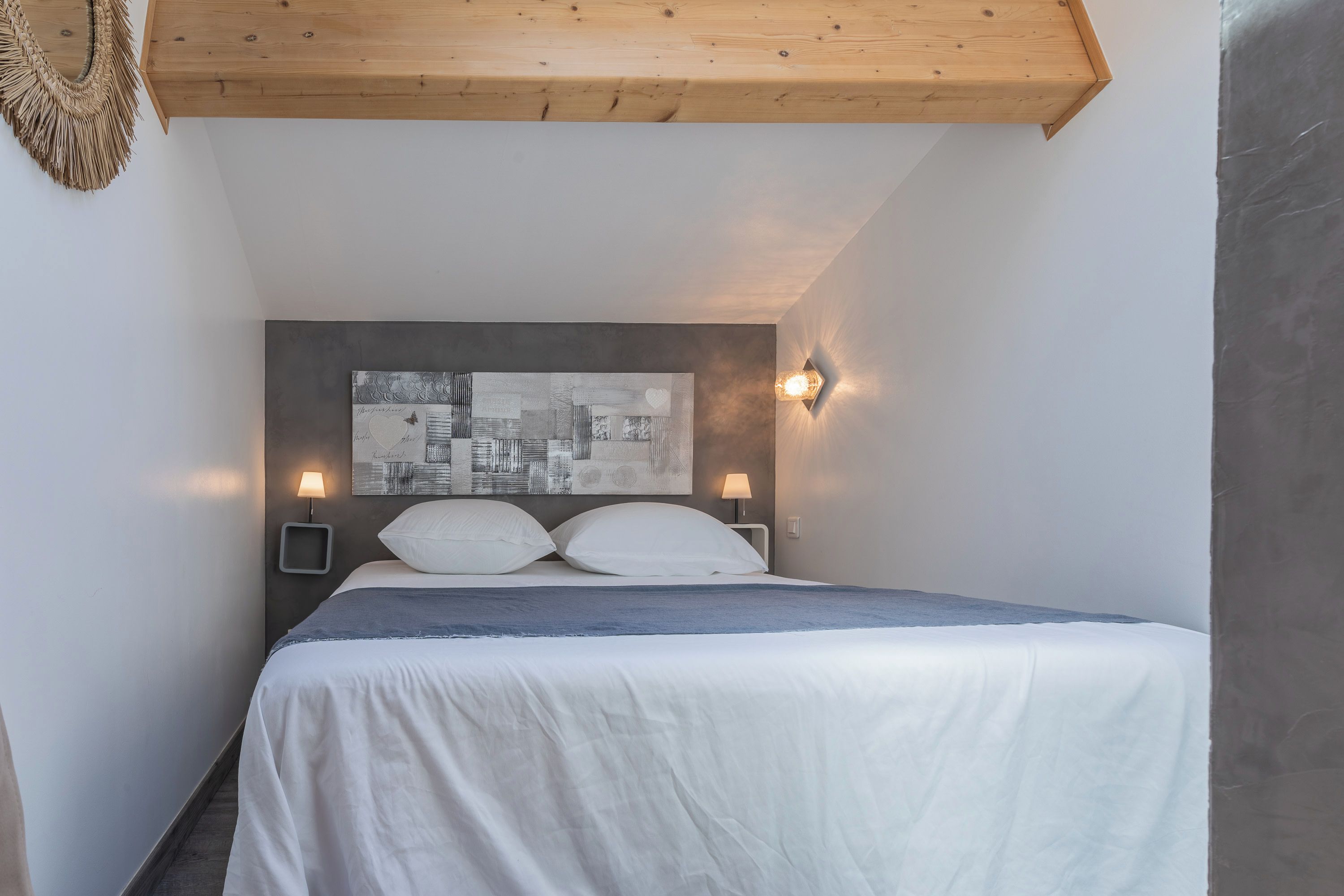 A bedroom with a bed, two bedside lamps, a cityscape artwork on the headboard, and a wooden ceiling.