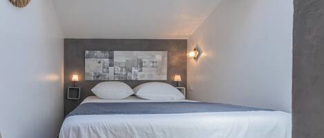 A bedroom with a bed, two bedside lamps, a cityscape artwork on the headboard, and a wooden ceiling.