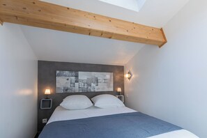 A bedroom with a bed, a wall-mounted artwork, two bedside lamps, and a sloped ceiling with exposed wooden beams. - Les Bois Flottès - Jardin -Climatisation (Poussan)