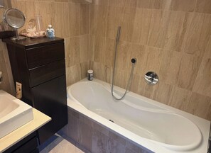 Un baño con bañera, tocador con espejo y artículos de aseo.