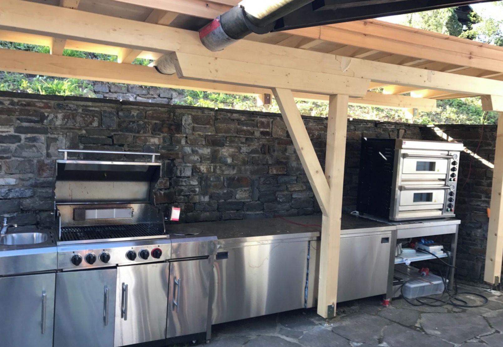 An outdoor kitchen with a stone wall backdrop, a built-in grill, and a pizza oven.