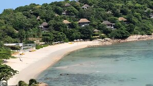 A coastal area with a sandy beach, clear water, and a hillside with multiple buildings. - "Villa by the Bay" with panoramic view of Samrong Bay and Koh Phangan island. (Chang Wat Surat Thani)