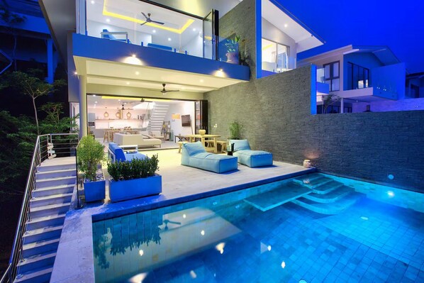 Una casa moderna de dos pisos con piscina, mobiliario exterior y una escalera que lleva a la planta alta.