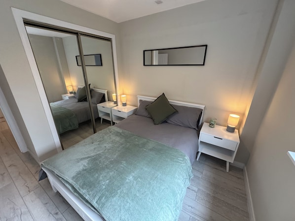 A bedroom with a bed, two bedside tables, a mirror, and a wall-mounted light fixture. - Newly Renovated 1 Bedroom Flat In Edinburgh - Sleeps 4 People (Edinburgh)