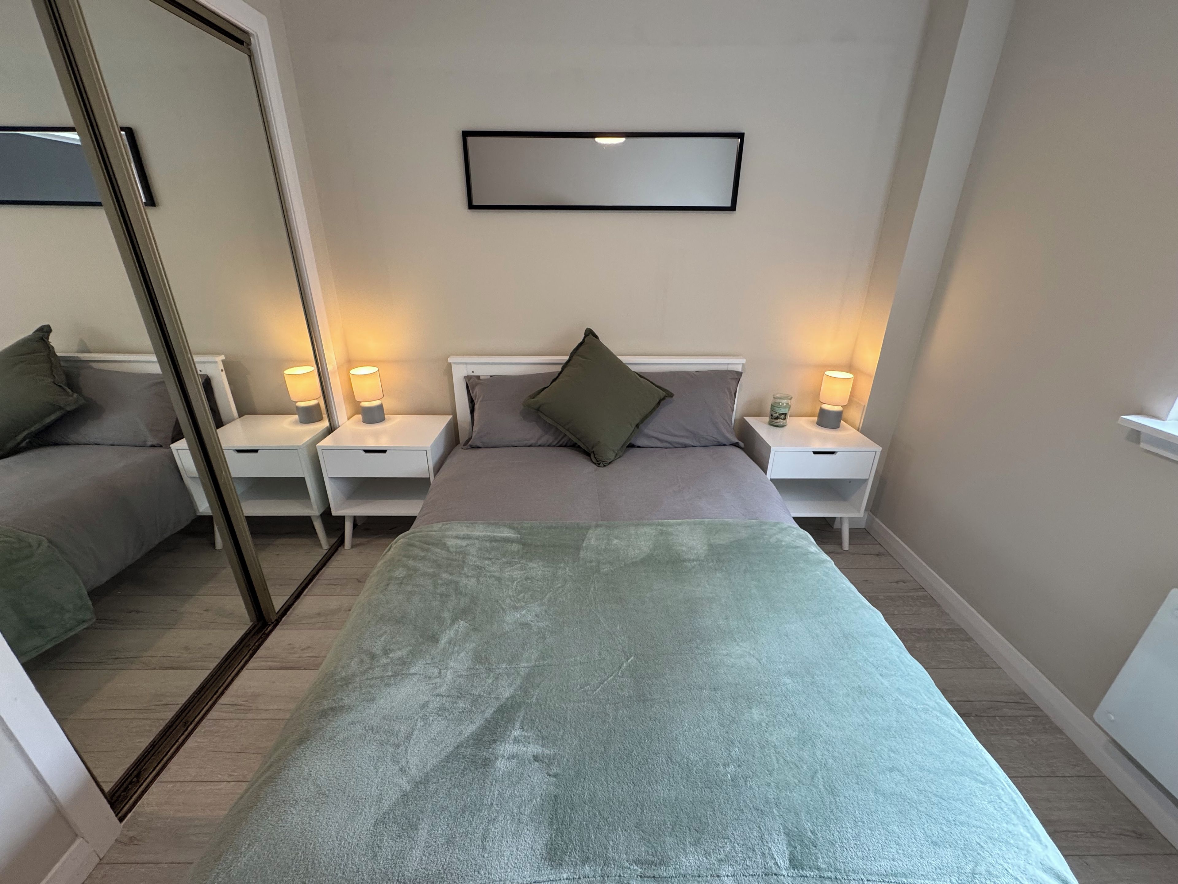 Un dormitorio con una cama, dos mesitas de noche, un tocador, un espejo y una lámpara de pared.