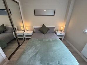 Une chambre à coucher comprenant un lit, deux tables de chevet, une commode, un miroir et un luminaire fixé au mur.